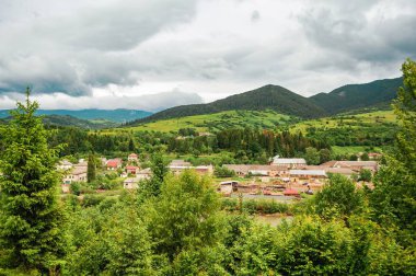 Köy yeşil yuvarlanan tepelerin ve uzak dağların arasına kurulmuş. Bu manzaralı gökyüzünün altında..