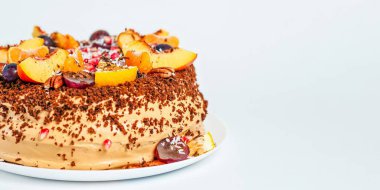 Taze meyve ve fındık çeşitleriyle süslenmiş güzel bir pasta, beyaz bir tabakta oturuyor, şenlikli bir ikram..