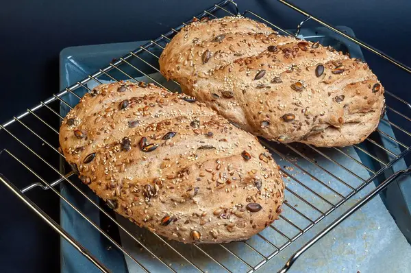 Soğutma rafında taze pişmiş iki somun ekmek, altın kabuklarını ve sağlıklı dokularını sergiliyorlar, tadını çıkarmaya hazırlar. Tohumlar görsel bir cazibe ekler..