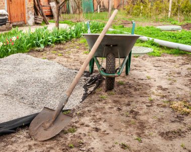 Bahçe aletlerinin bir görüntüsü, bir kürek ve el arabası dahil, bir yığın çakılın yanında, peyzaj çalışması için hazır..