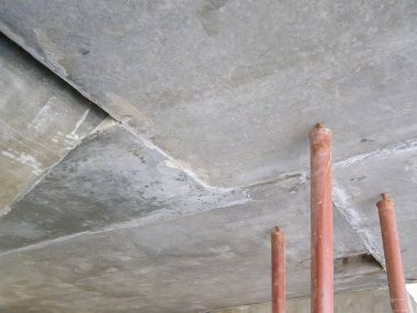 Endüstriyel bir ortamda destek direkleriyle beton bir tavan manzarası. Görüntü inşaat detaylarını yakalar.