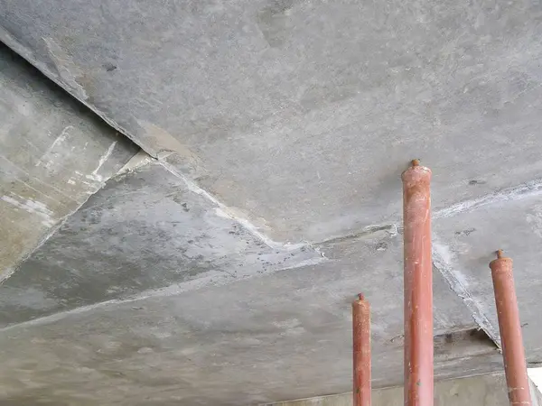 Endüstriyel bir ortamda destek direkleriyle beton bir tavan manzarası. Görüntü inşaat detaylarını yakalar.