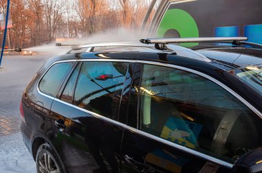 Araba yıkamada siyah bir araba yıkanıyor, çatıya su püskürtülüyor. Araba parlak ve temiz..