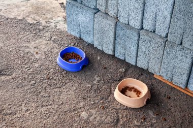 Köpükle dolu iki evcil hayvan kasesi bir yığın inşaat bloğunun yanında oturur ve açık hava beslenmesini ima eder..