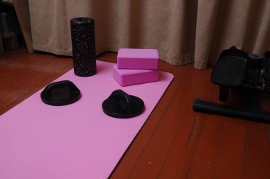 Pembe paspasın üzerindeki yoga ekipmanları, köpük silindirler, bloklar ve şınav çubukları, egzersiz için hazır bir ev çalışması sahnesi yaratır..