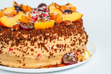 Çok güzel dekore edilmiş, şeftali ve üzümlü taze meyvelerle süslenmiş bir pasta. Pasta arka planda beyaz bir tabakta sunuluyor..