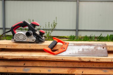 Bir elektrikli planör ve el testeresi ahşap bir deste üzerinde dinleniyor bir çit ve yeşillik karşı, ahşap işçiliği için hazır.