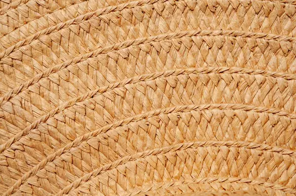 Örülmüş hasır bir şapkanın yakın plan çekimi, karmaşık dokusunu ve doğal rengini gözler önüne seriyor. Güneşin öptüğü saman deseni çok güzel görünüyor..