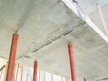 İnşaat sırasında yukarı doğru bir açıyla çekilen, kırmızı metal aksesuarlarla desteklenen beton bir levhanın göz hizasında çekimi. Levha yüzeyinde aşınma izleri var..