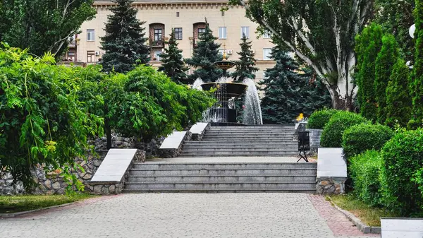 Çeşme, merdiven, yeşillik ve arka planda huzurlu bir şehir manzarası yaratan manzaralı bir açık hava çekimi..