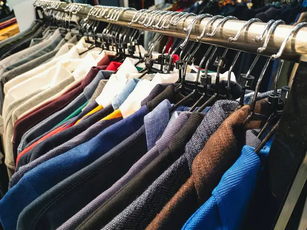 Askılarda asılı çeşitli renkli kıyafetlerin yakın çekimi, bir giyim mağazasının seçimini gözler önüne seriyor.