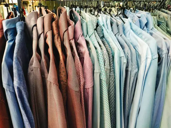 Askıda asılı bir gömlek koleksiyonu, çeşitli renkler ve desenler sergiliyor, alışveriş ve moda için mükemmel..