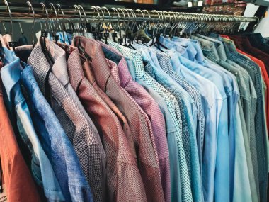 Renkli bir erkek gömleği dizisi, çeşitli desenler ve renkler içeren bir elbise askısına asılmış..