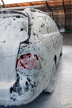 Bir araç, araba yıkama yerindeki yoğun, beyaz köpükle kaplıdır. Arka lambanın yanındaki temizlik işlemini gösterir..