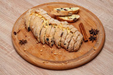 Kızılcık ve fındıklı dilimlenmiş bir bisküvi, yıldız anason ve tarçın çubuklarıyla süslenmiş ahşap bir tahtanın üzerinde oturur. Tatlı, kırsal bir dokunuşla yakın plan çekimdir..