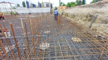 İnşaat sahasında, arka planda işçilerin yer aldığı beton döşemeye hazır bir inşaat iskeleti ortaya çıkarılıyor. Temel inşa ediliyor..