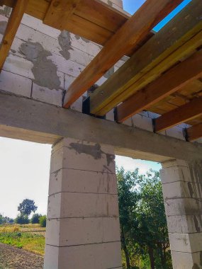 Tahta kirişleri, betonu ve duvarları içeriden görülebilen tamamlanmamış bir yapı. Gökyüzü bitmemiş çatıdan görülebiliyor..