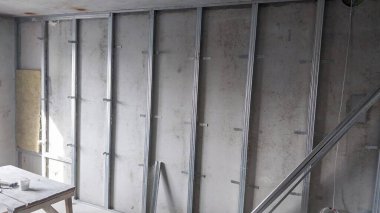 Bu resim inşaat halindeki bir duvarı gösteriyor, metal çiviler ve yalıtım kısmen yerleştirilmiş, alçıpan veya diğer tamamlama materyalleri için hazır..