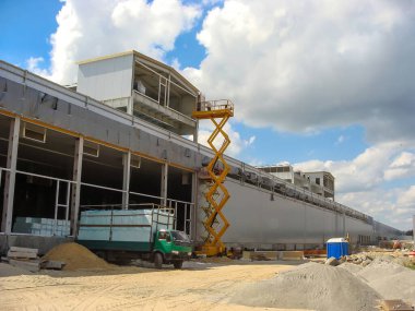 İnşaat alanına park etmiş yeşil bir kamyon, makas kaldıracı ve bulutlu bir gökyüzünün altında tamamlanmamış bir bina..