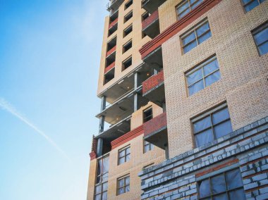 Arkasında açık mavi gökyüzü olan inşaat halindeki bir binanın mimari görüntüsü. Tamamlanmamış katlar var..