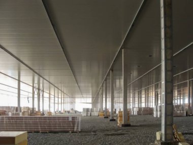 Bu geniş iç mekan birçok gri destek sütunu barındırıyor ve inşaat malzemeleriyle çakıl zeminde projenin tamamlanması için hazırlanıyor..