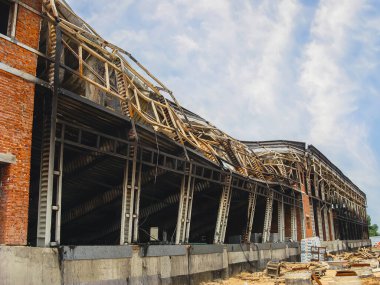 Çökmüş çatılı hasarlı bir bina ve yangından sonra görülebilir yapısal hasar, bulutlu bir gökyüzüne karşı kurulmuş..