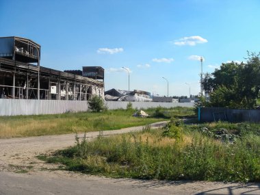 Hasarlı cepheli yanmış bir endüstriyel binanın dış görünüşü. Sahne berrak, mavi bir gökyüzünün altında geçiyor..