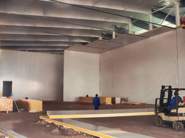 İnşaatı devam eden bir depoda. İşçiler ve bir forklift görülebilir, malzemeler tüm uzaya dağılmış durumda..