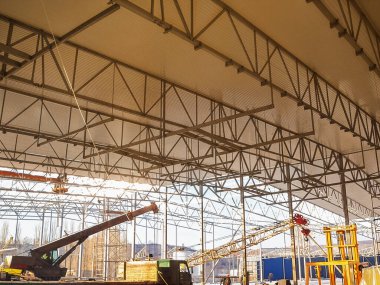 Metal iskelet çatısı altında vinç ve makinelerin kullanıldığı büyük bir yapının içini gösteren bir inşaat alanı.