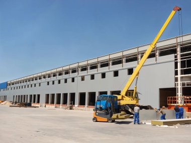 İnşaat alanı vinç, forklift ve işçiler güneşli bir günde bir bina kurarak endüstriyel ve inşaat sürecini yakalıyorlar..
