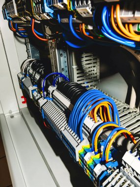 Renkli kablolar ve devrelerle, güç dağılımını ve kontrol sistemlerini gösteren bir elektrik panelinin yakın çekimi.