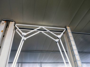 Göz hizasındaki bir görüntü, çelik destek kirişlerini bükülmüş metal bir tavana yansıtıyor. Güçlü çizgiler ve geometrik şekiller hakim.