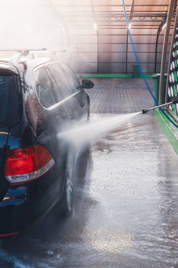 Bir oto yıkama tesisinde yüksek basınçlı su spreyi ile yıkanan siyah bir araba. Su bir sis yaratır..