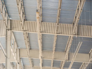 Metal çatının karmaşık yapısını gösteren bir mimari çekim, kirişleri ve kıvrımlı panelleri geometrik desenler oluşturuyor..