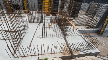 Tepeden çekilen bir çekim, bir inşaat alanının karmaşık çerçevesini yakalar, arka planda biçimlendirme ile metal demiri ve beton temeller sergilenir.