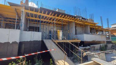 Güneşli bir günde inşaat halinde olan bir bina, beton duvarlar ve açık mavi gökyüzü ile iskeleyi gösteriyor..