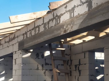 Açık tuğla, ahşap kirişler ve parlak bir gökyüzüne karşı merdiven gösteren bir binanın yakın çekim görüntüsünü yakalıyor..