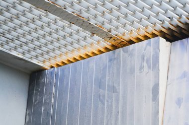 Endüstriyel bir sahnede metal rendeleyici, kıvrımlı paneller ve pas izleri var. Dokular ve desenlerle ilginç bir kompozisyon oluşturuyor..