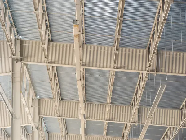 Metal çatının karmaşık yapısını gösteren bir mimari çekim, kirişleri ve kıvrımlı panelleri geometrik desenler oluşturuyor..