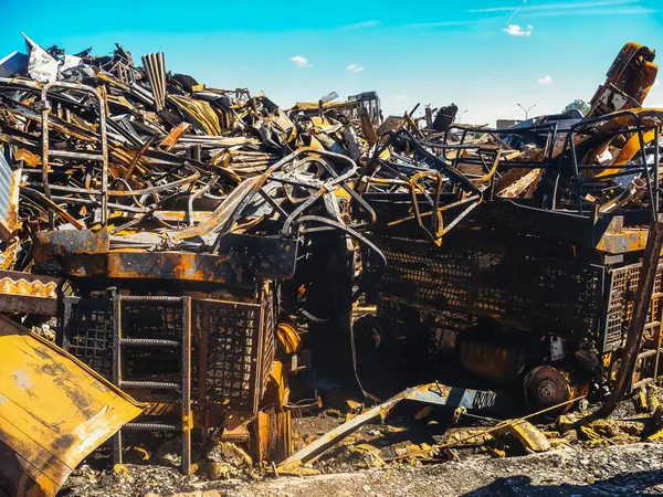Bir aracın enkazının detaylı bir görüntüsü, muhtemelen bir inşaat ya da endüstriyel makine, yangından sonra, mavi gökyüzü altında kömürleşmiş metal ve enkaz ile.