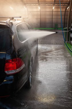 Siyah bir araba, bir oto yıkama tesisinde detaylı bir temizliğe tabi tutulur. Suyun detaylarıyla yakalanır..