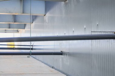 Metalik elementler, borular ve yapısal desteklerle modern bir endüstriyel iç yapı, mimari ayrıntıları sergiliyor.