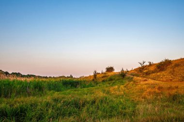 Şafak veya alacakaranlıkta bir tepe, çimen ve eğimli bir gökyüzü barındıran güzel bir manzara..