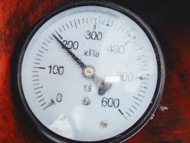 Gösterge KPa 'da basınç ölçümleri gösteriyor. Siyah bir iğne 200' e işaret ediyor. Arka planda kırmızı metalik bir yüzey var..