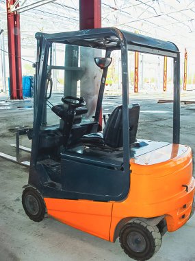 An orange forklift stands in a construction site, with the building's frame visible in the background, ready for work.