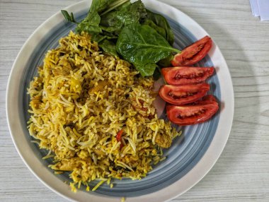 Biryani made from spices, vegetables, chicken and other ingredients and served with side of salad made from baby spinach and tomatoes.