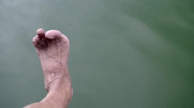 Egzersiz yapan ve nehir kenarında ayaklarını esneten bir adam..