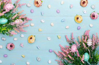 Easter composition of pink spring flowers, colorful roses, cute bunnies and decorative eggs. Advertising content for Easter holiday on blue wooden background. Flat lay, top view, close up