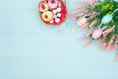 Easter composition of pink spring flowers, colorful roses, cute bunnies and decorative eggs in a nest. Content for Easter holiday on blue wooden background. Flat lay, top view, close up, copy space