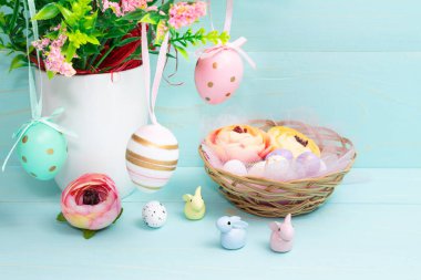 Easter composition of pink spring flowers, colorful roses, cute bunnies and decorative eggs in a nest. Content for Easter holiday on blue wooden background. Flat lay, side view, close up, copy space